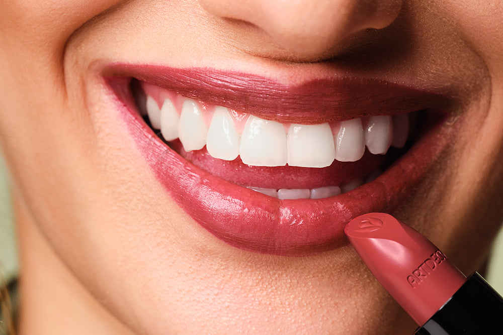 Geschminkte Lippen werden gezeigt, wobei ein Lippenstift vor das Gesicht gehalten wird