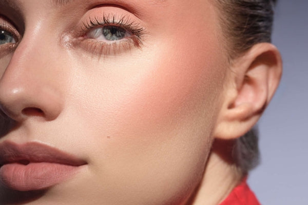 Nahaufnahme eines frischen Make-up-Looks mit samtigem Teint, roséfarbenem Blush und natürlichem Wimpernaufschlag für einen ebenmäßigen Glow-Look.