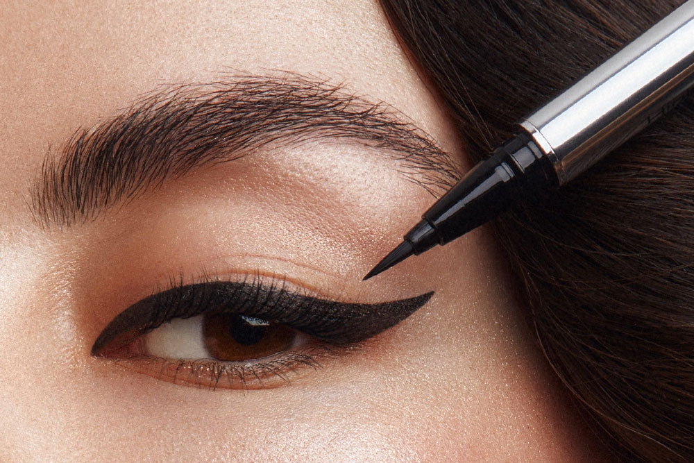Ein Eyeliner wird vor einem geschminktem Augen gehalten