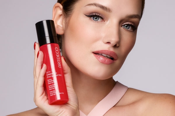 Model hält das 3 in 1 Make-up Fixing Spray an ihre Wange und lächelt dabei glücklich
