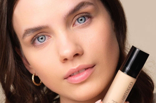 Model hält die Perfect Teint Foundation und blickt mit leicht geneigtem Kopf neutral in die Kamera.