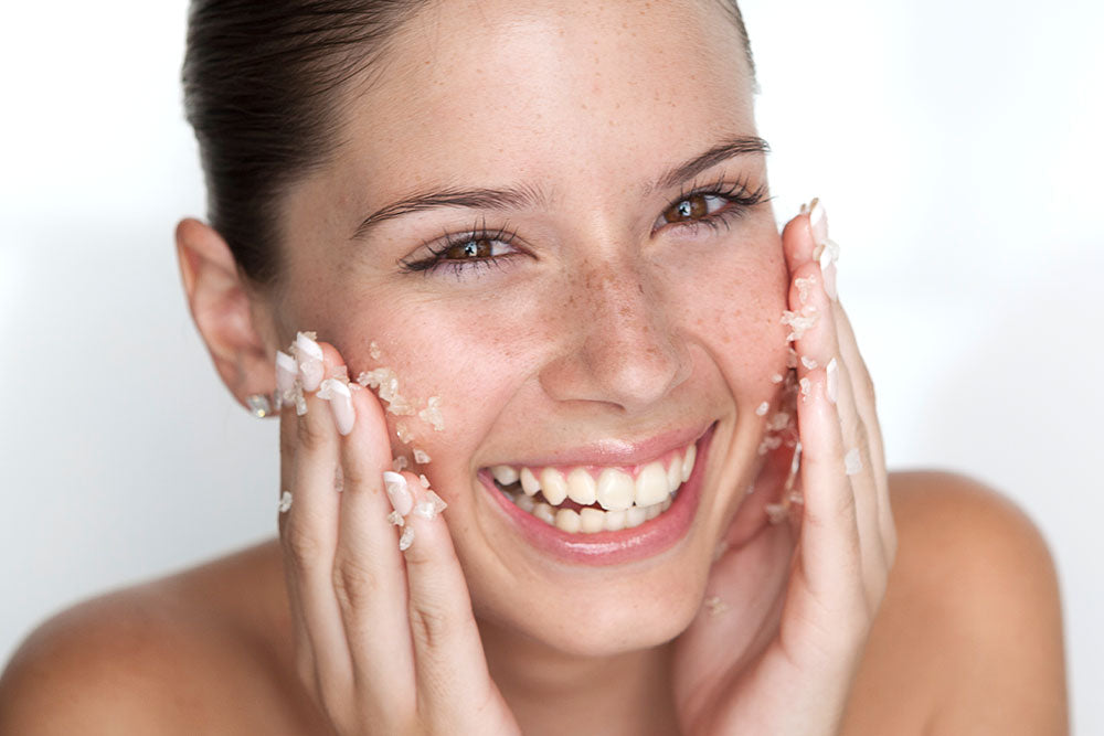 Eine weibliche Person reibt ihr Gesicht mit einem Peeling ein