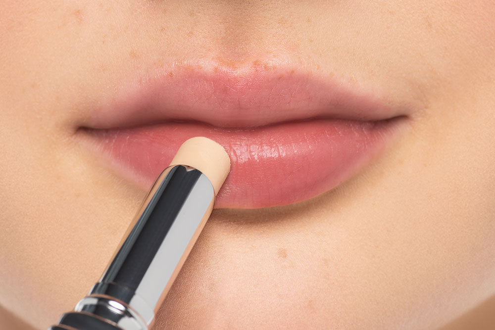 Lippen in Nahaufnahme und ein Pflege-Lippenstift wird vor den Lippen gehalten