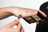 Es wird eine Hand gezeigt die eine befüllte Palette in der Hand hält und sich mit einer Spatel Camouflage auf die Hand aufträgt