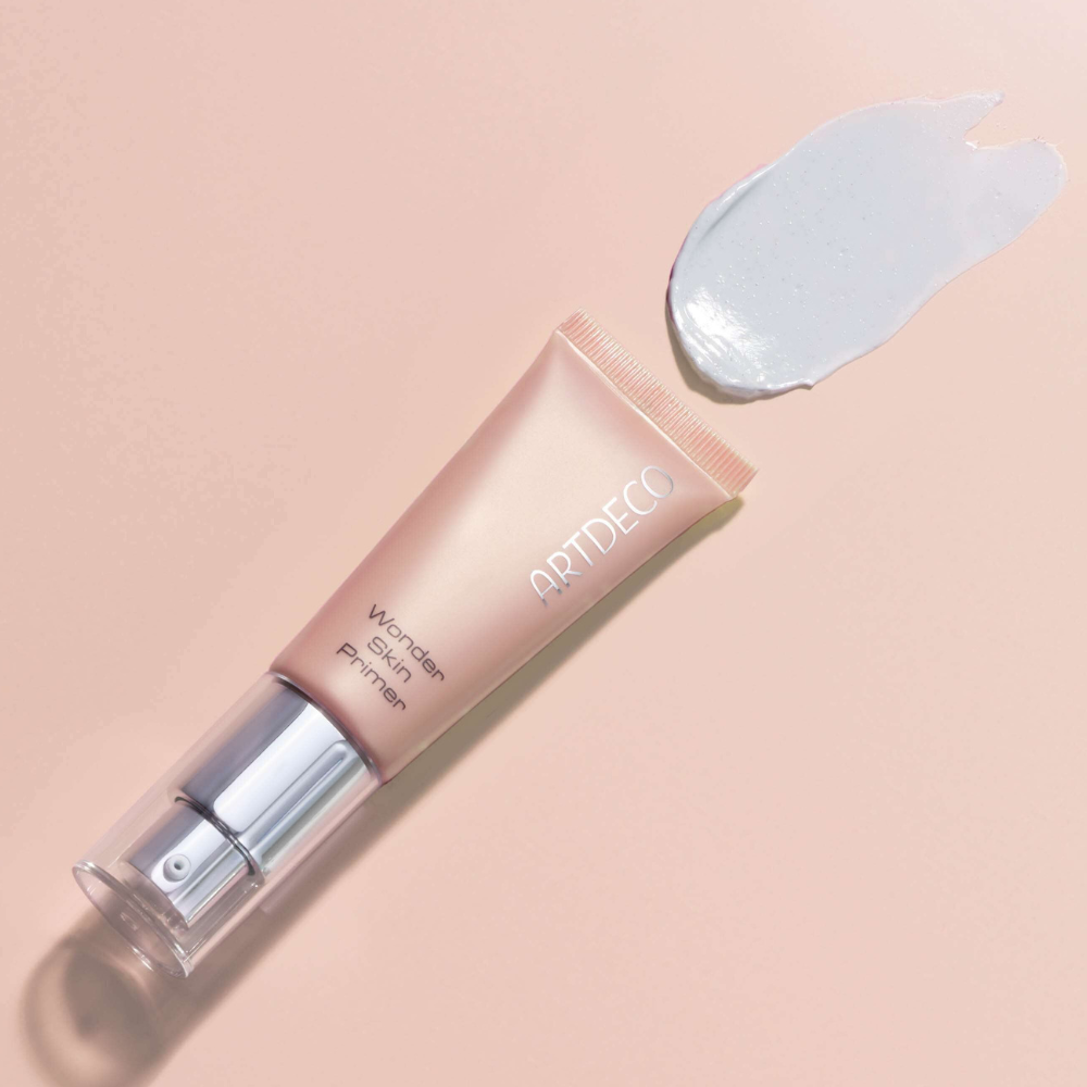 Wonder Skin Primer liegt auf einem hellrosa Hintergrund mit einem Textur Swatch des Produktes