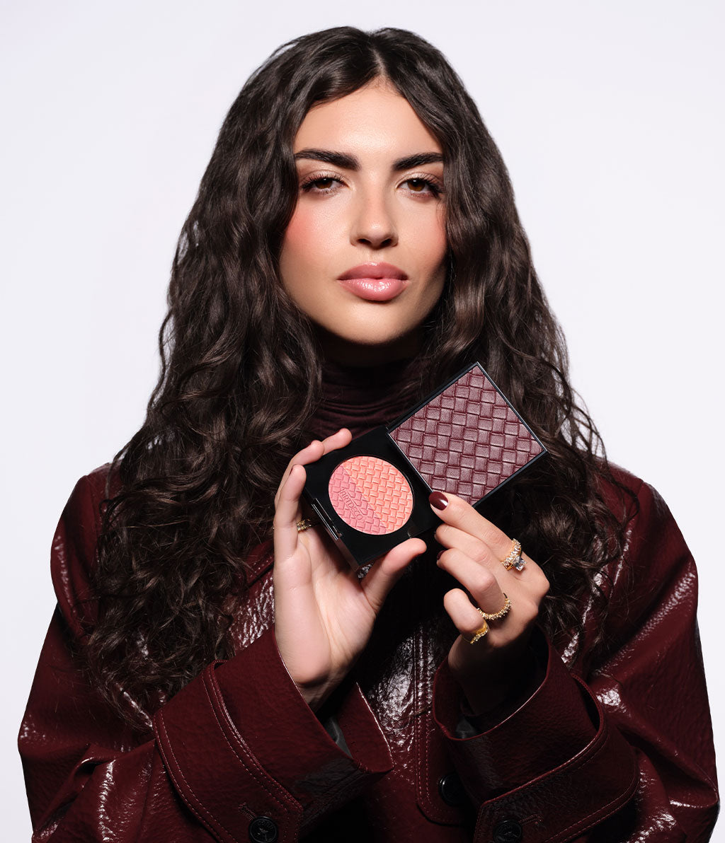 Brünettes Model trägt eine weinrote Jacke und hält den geöffneten Blush Couture in der Hand, sodass man Prägung und das Intrecciato-Design gut sichtbar ist.