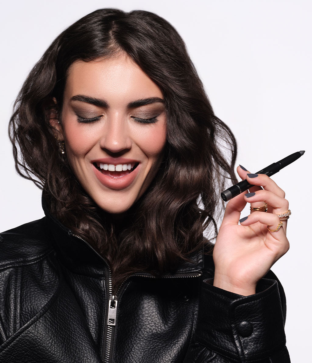 Brünettes Model in schwarzer Jacke und herbstlichen Make-up, hält den High Performance Eyeshadow Stylo N°02 in der Hand.