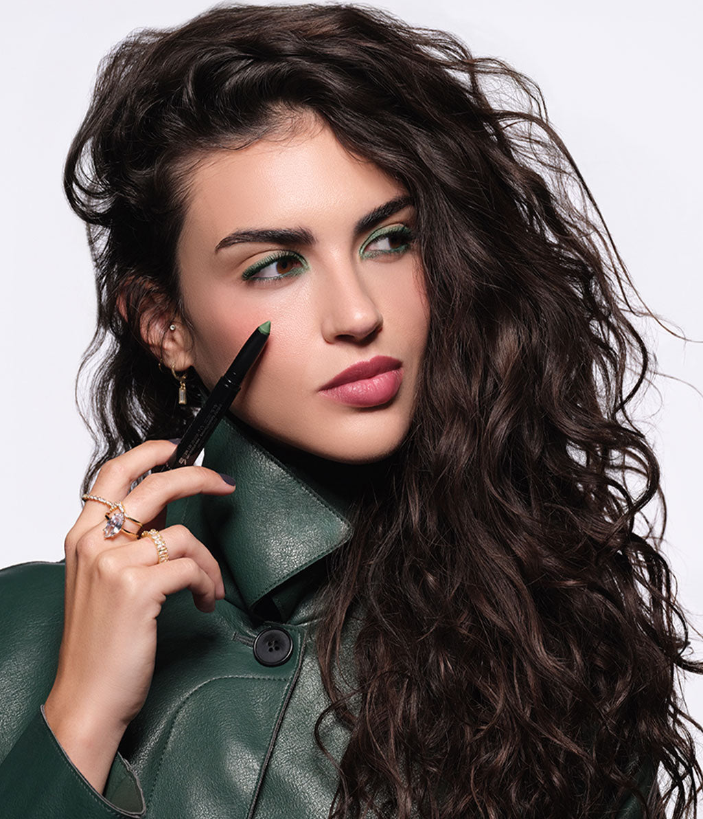 Brünettes Model in grüner Jacke und herbstlichen Make-up, hält den High Performance Eyeshadow Stylo N°80 in der Hand.