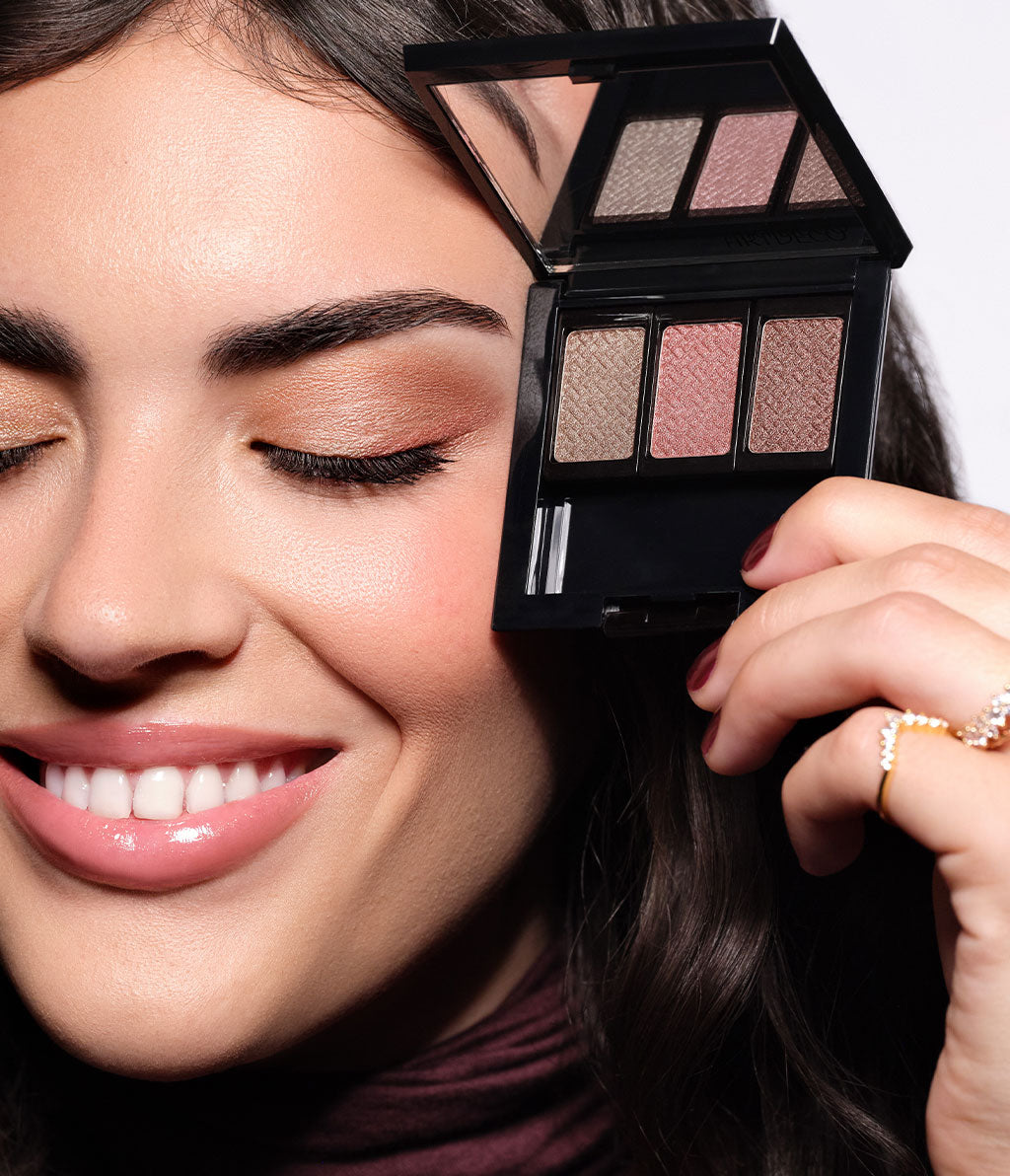 Brünettes Model hält die geöffnete Beauty Box mit den Lidschatten aus der  Kollektion neben dem geschminkten Auge.