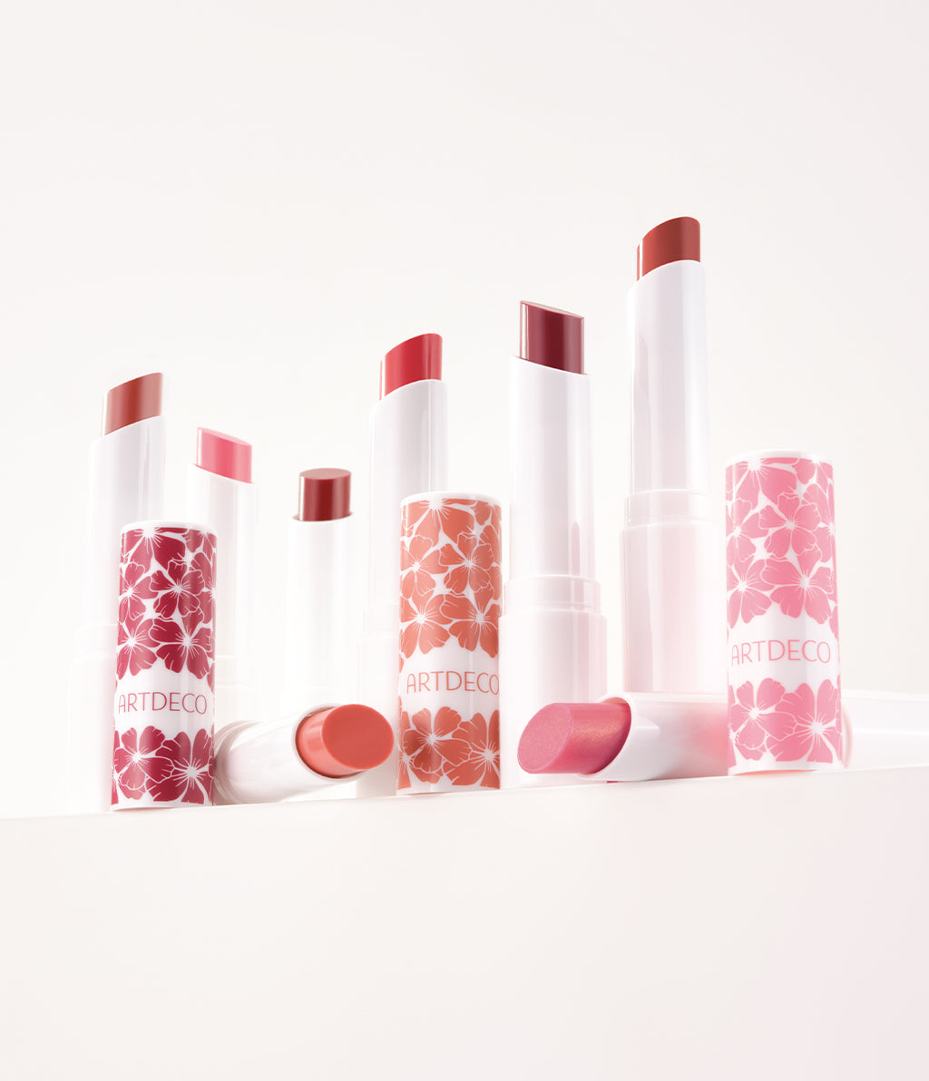 Alle acht Farben des Color Booster Lip Balm im limitieren Blumen-Design werden auf einem weißen Hintergrund hochwertig präsentiert