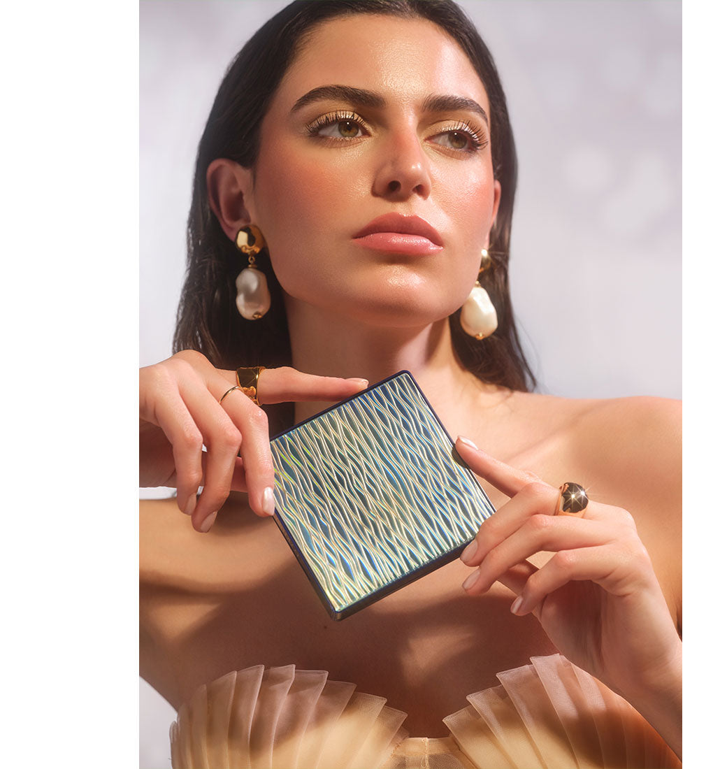 Brünettes Model mit einem sommerlichen und glowy Make-up, hält das All Seasons Bronzing Powder in den Händen, sodass man die wellenartige Verpackung gut erkennen kann