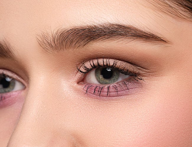 Es wird ein geschminktes Auge mit violettem Lidschatten gezeigt
