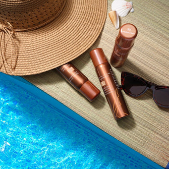 Sommerliches Bild der Spray On Leg Foundation mit Sonnenhut und Muscheln am Poolrand.