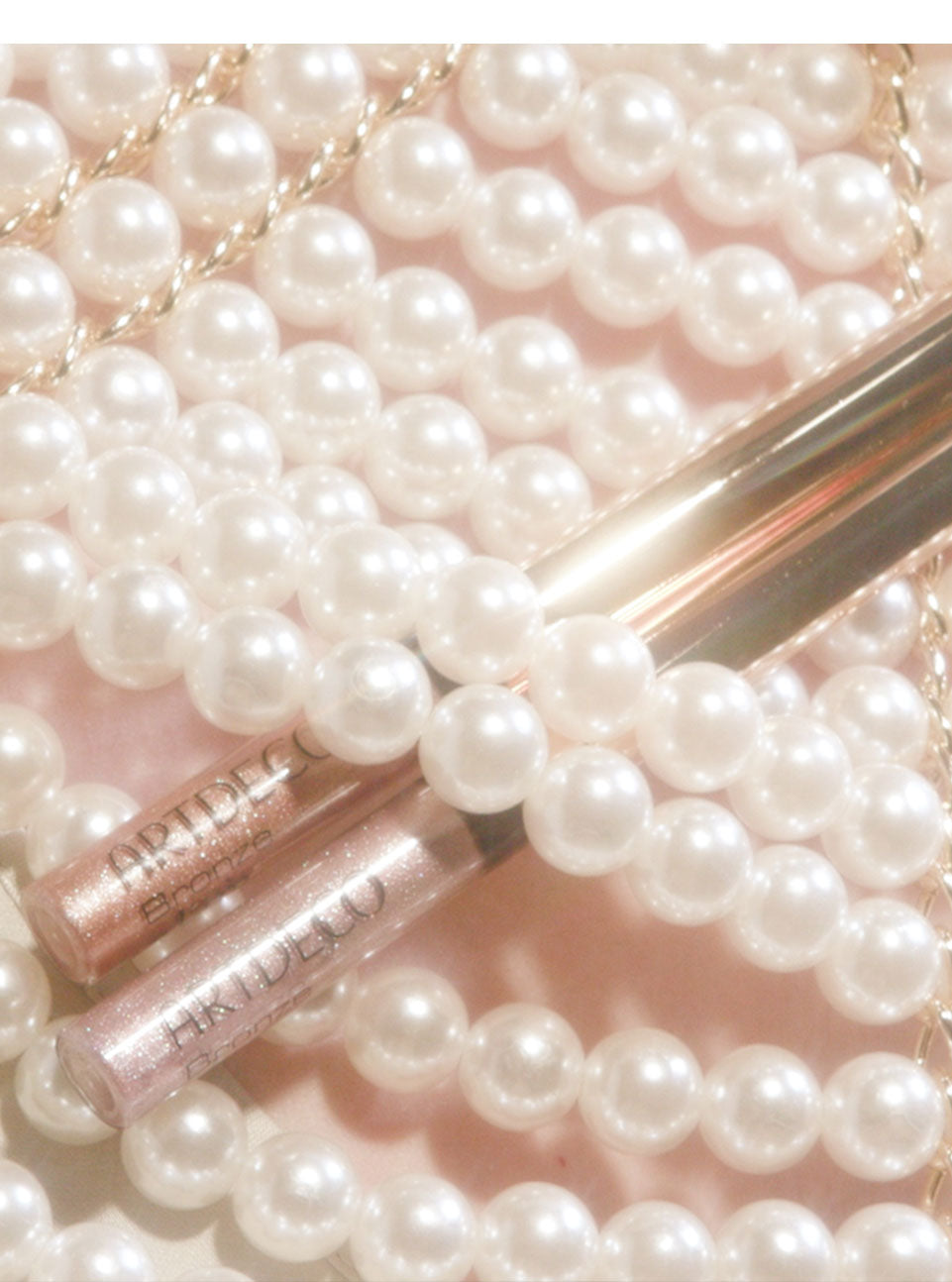 Die beide neuen Bronze Glam Eye Liner aus der Mermaid Kiss-Kollektion sind ästhetisch hinter ein paar Perlen platziert 
