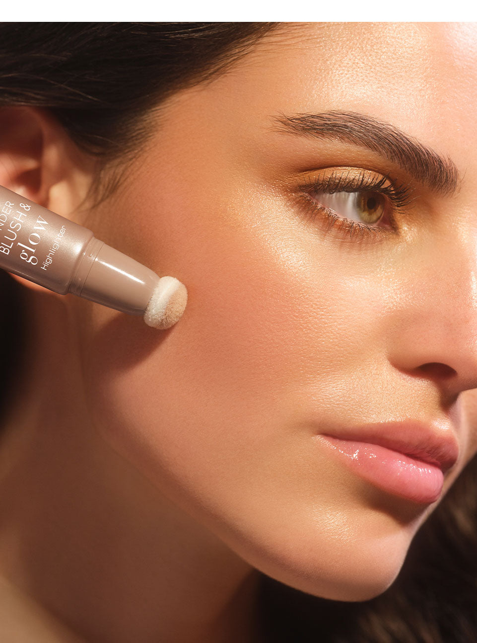 Brünettes Model mit glowy Make-up trägt den Wonder Blush & Glow Highlighter mit dem Schwämmchenapplikator auf ihre Wange auf, und dieses Ergebnis zu erzielen