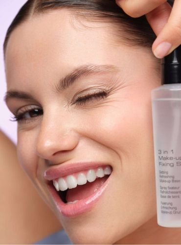 Model hält Fixing Spray in der Hand und lächelt verspielt in die Kamera