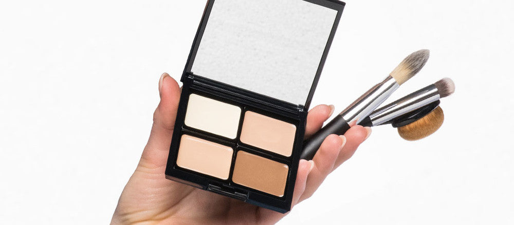 Hand hält Beauty Box mit vier verschieden Camouflage Creams und für das Produkt geeignete Pinsel