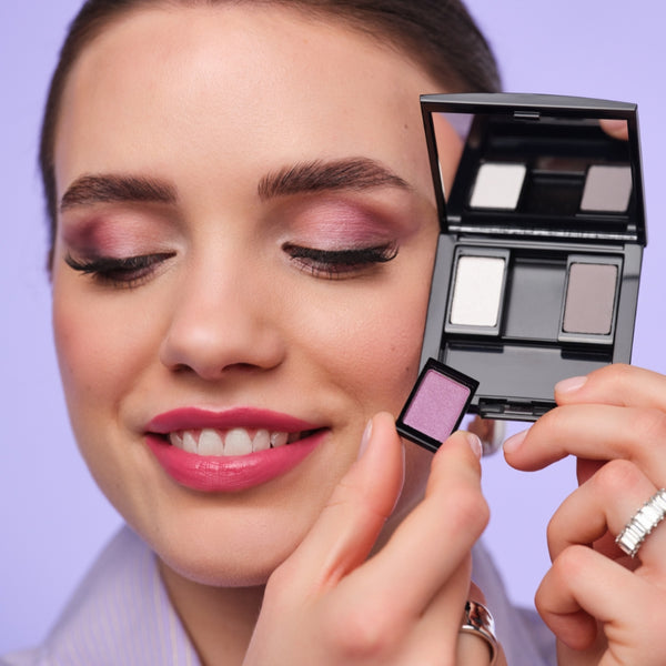 Model mit zartem Abend-Make-up in Flieder und Rosé zeigt eine befüllte Beauty Box.