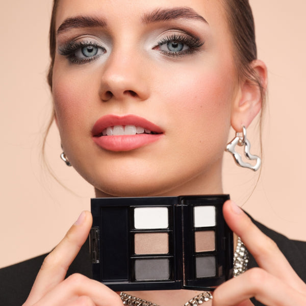Model mit intensivem Augen-Make-up in Schwarz, Grau und Silber trägt voluminöse Wimpern und zeigt eine befüllte Beauty Box.