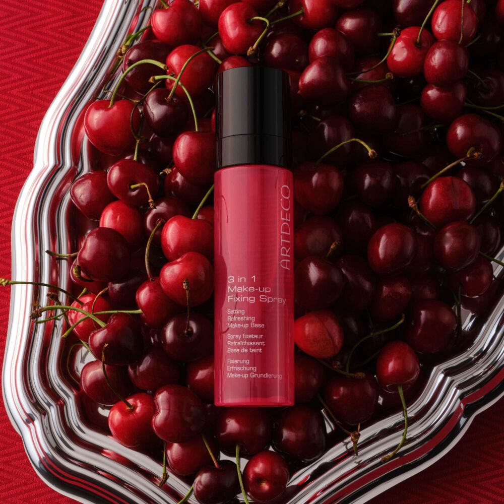 3 In 1 Make-up Fixing Spray platziert auf roten Kirschen, passend zum neuen roten Packaging des Produkts.